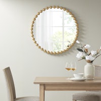 a round gold mirror hangs above a dining table